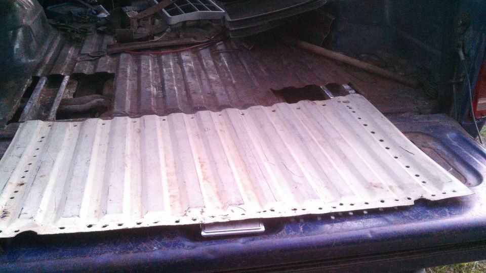 Truck bed with a corrugated metal panel lying on the floor, showing rust and damage