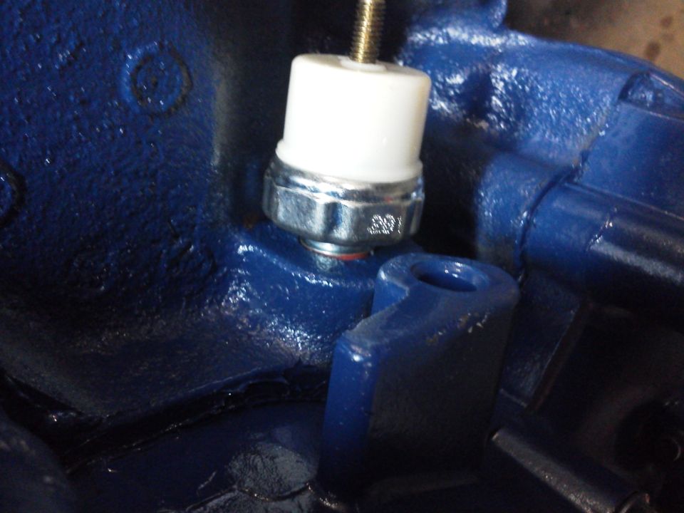 Close-up of an oil pressure sending unit with "391" visible on its metal housing, mounted on a blue-painted engine component