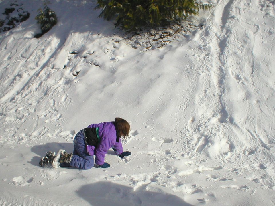 Child in purple jacket and blue snow pants kneeling in snow