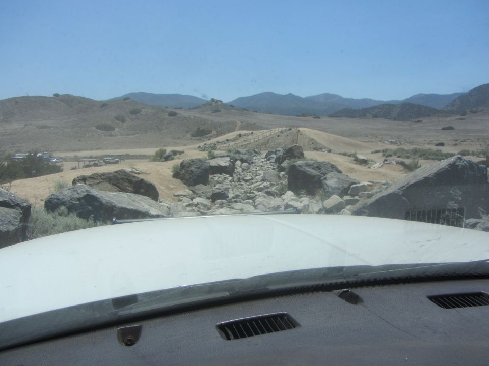 White hood and dashboard view of a rocky, hilly landscape under a clear blue sky