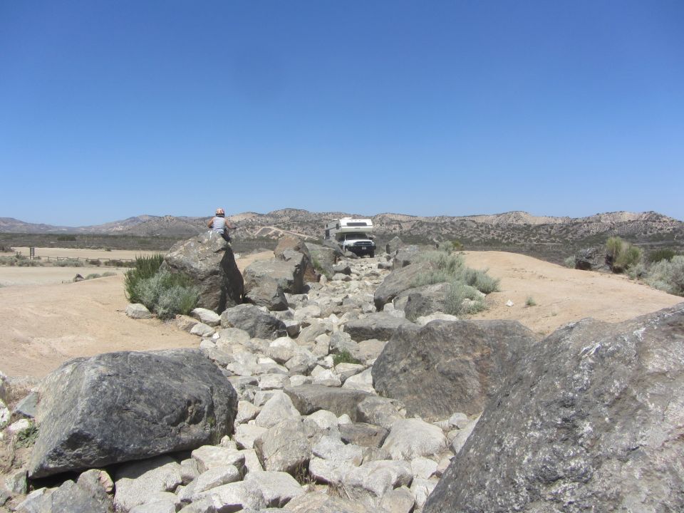 RV driving on a rocky path with a person sitting on a boulder