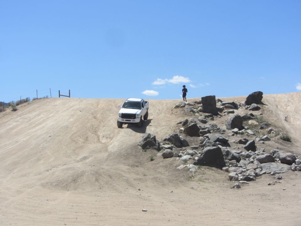 White pickup truck driving down a dirt hill with a person standing on top
