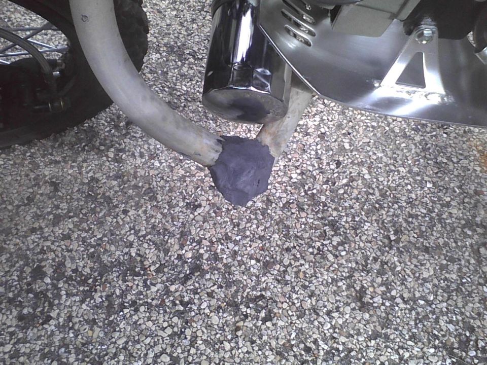 Close-up of a motorcycle's exhaust pipe with some dark putty applied where it connects