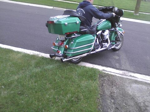 2003 Ford Crown Victoria - A rider on a green motorcycle is seen from the rear, parked on the side of a road.