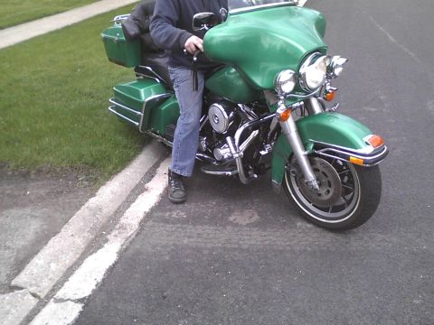 2003 Ford Crown Victoria - A green motorcycle with saddlebags is parked on the side of the road, with a person seated on it.