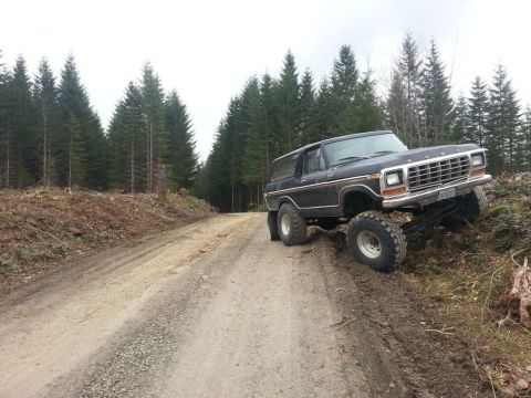 1979 Ford Bronco - This lifted black Ford Bronco is navigating a rough dirt road in a wooded area.