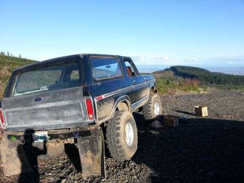 1979 Ford Bronco - A modified 1978 Ford Bronco sits on a rocky terrain under a clear blue sky, with a distant forest visible.