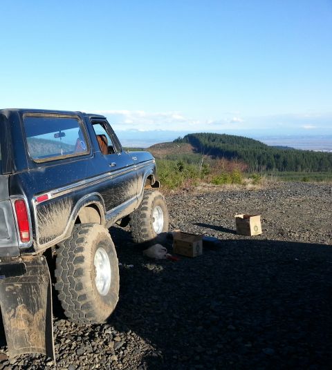 1979 Ford Bronco - A lifted black 1979 Ford Bronco is parked on a rocky incline with a scenic view of hills and mountains in the background.