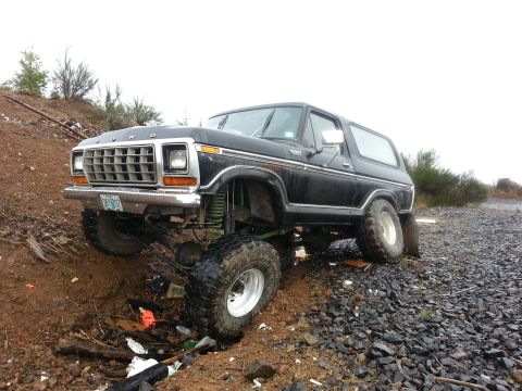 1979 Ford Bronco - This modified Ford Bronco is navigating a challenging off-road terrain with one wheel in a ditch.