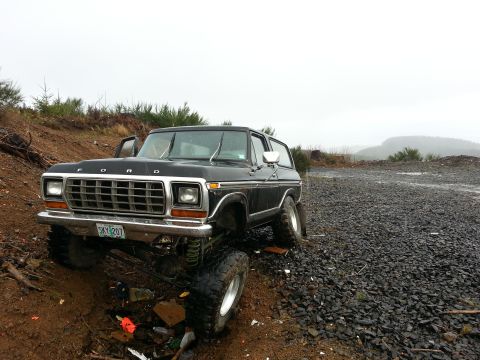 1979 Ford Bronco - This lifted Ford Bronco is parked on a rough, off-road terrain with a cloudy sky overhead.
