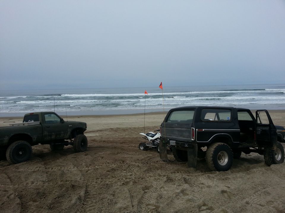 Black 1979 Ford Bronco with open door and quad bike on beach