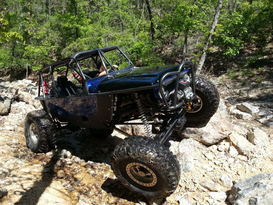 Off-road buggy with large tires climbing over rocks on a wooded trail