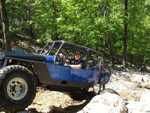 1967 Ford Mustang - A blue off-road buggy with a roll cage is driven by a man through a wooded, rocky area.