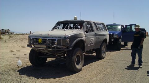 1996 Ford Bronco - A gray and black off-road race Ford Bronco marked with number '50' sits on a dusty desert lot, fitted with a roll cage, tube front bumper,…