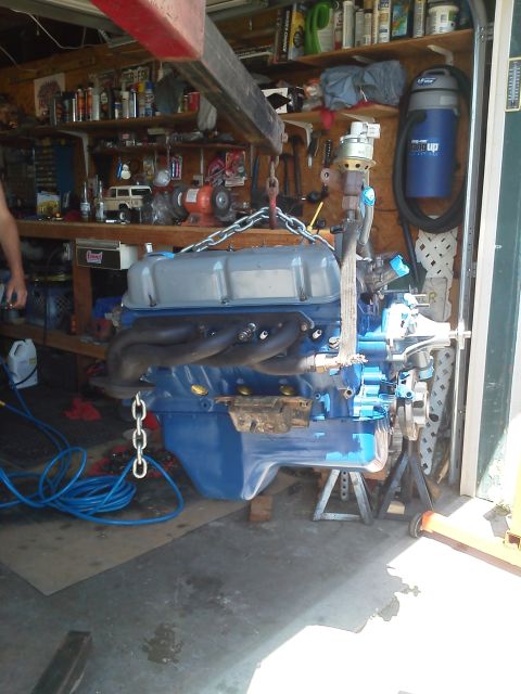 1988 Ford Bronco - A blue engine with silver valve covers is suspended by a shop crane, ready for installation or removal.