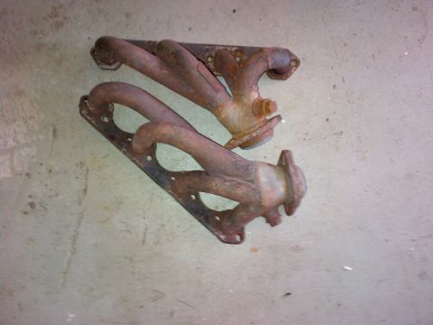1994 Ford Bronco - A pair of used exhaust manifolds, showing signs of rust and wear, lie on a concrete surface.