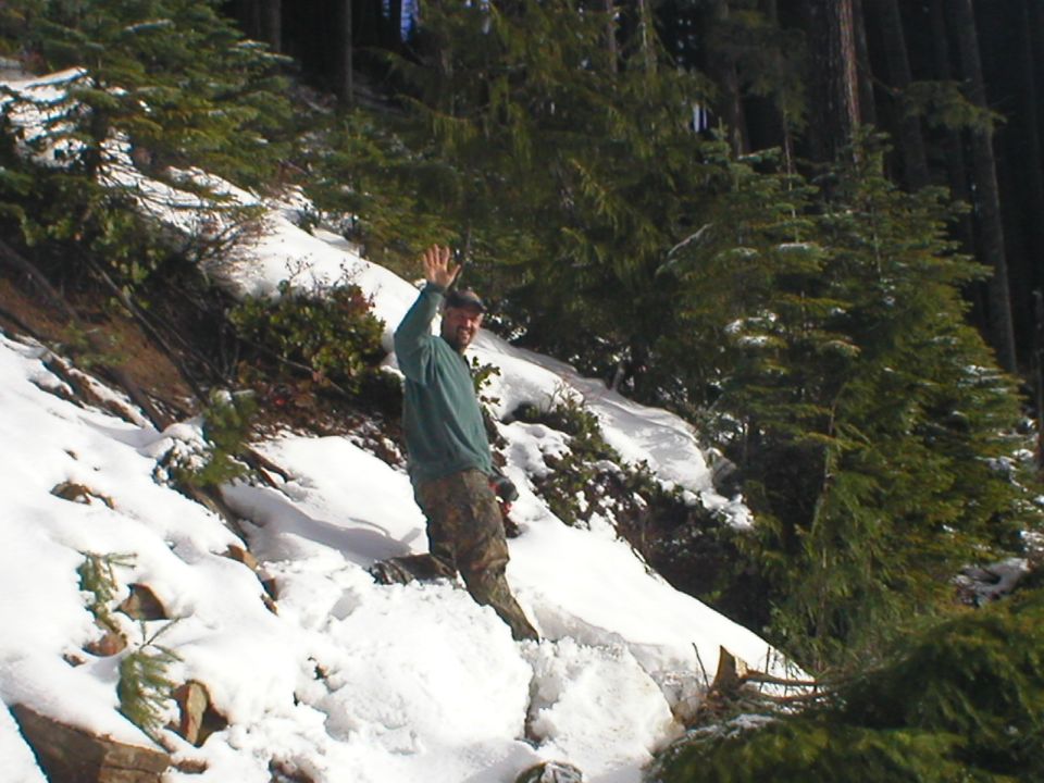 Man waving on snowy hillside with pine trees