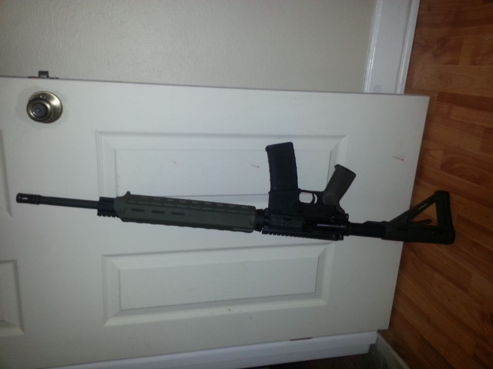 Assault rifle with extended magazine resting on a white door