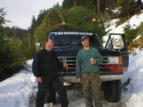 1978 Ford Bronco - Two men with a large Christmas tree loaded onto a truck in a snowy, wooded area.