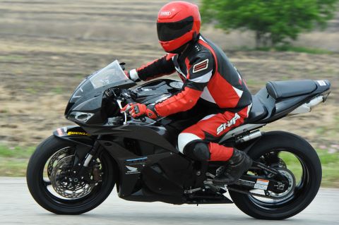 2001 Kawasaki KZ1000-A1 - A motorcyclist wearing a red helmet and racing suit rides a black sportbike on a paved road.