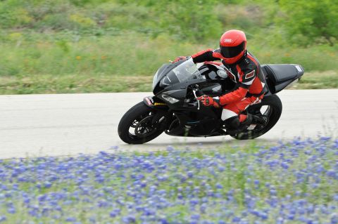 2001 Kawasaki KZ1000-A1 - A rider in red gear leans into a turn on a black sport motorcycle on a track bordered by bluebonnets.