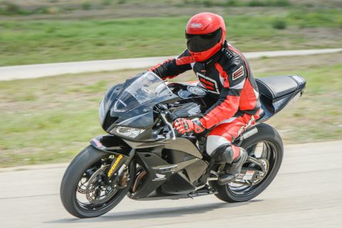 2001 Kawasaki KZ1000-A1 - A motorcycle racer in full gear navigates a turn on a paved track, with grassy areas visible in the background.
