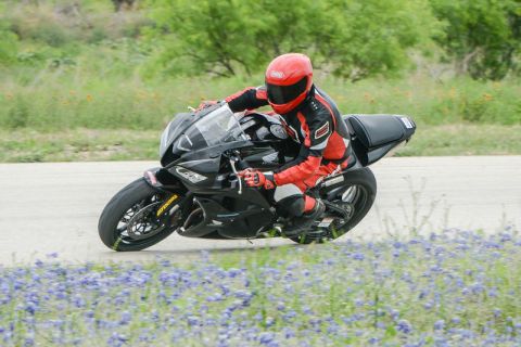2001 Kawasaki KZ1000-A1 - A motorcycle rider takes a turn on a track, with a field of bluebonnets visible.