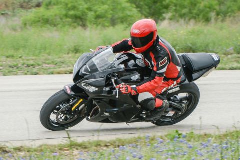 2001 Kawasaki KZ1000-A1 - A rider in full gear navigates a turn on a black sport motorcycle on a paved track with grassy verges.