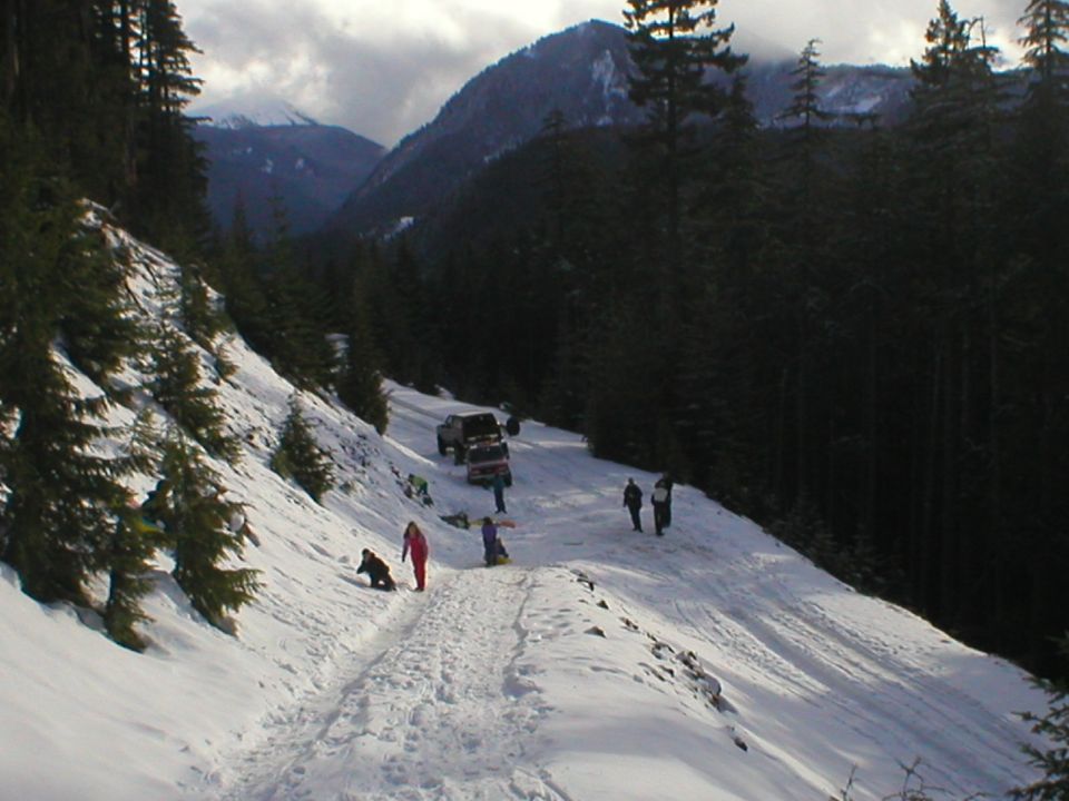 1978 Ford Bronco and other SUVs on a snowy mountain road with people sledding