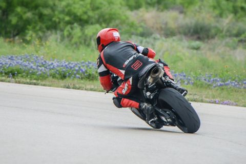 2001 Kawasaki KZ1000-A1 - A motorcycle and rider in full racing gear lean into a corner on a track surrounded by greenery.