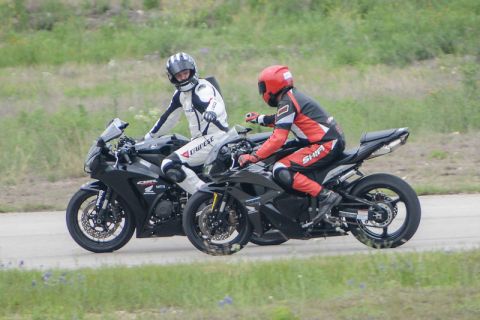 2001 Kawasaki KZ1000-A1 - Two sport motorcycles and their riders are seen on a track, with one rider in white and the other in red gear.