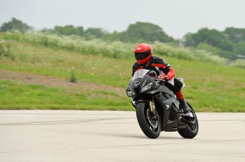 2001 Kawasaki KZ1000-A1 - A rider in protective gear maneuvers a black sportbike on a paved surface with a grassy embankment in the background.