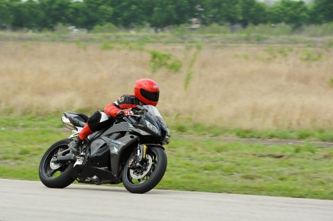 2001 Kawasaki KZ1000-A1 - Rider on a black sportbike takes a corner on a track with a grassy shoulder and distant trees.