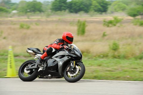 2001 Kawasaki KZ1000-A1 - A motorcycle rider in full gear navigates a turn on a paved track, with a yellow cone visible on the left.