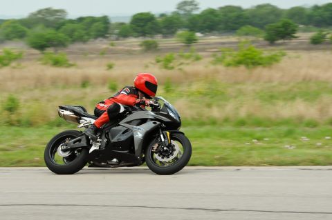 2001 Kawasaki KZ1000-A1 - A rider in red gear speeds along a road on a black sport motorcycle.