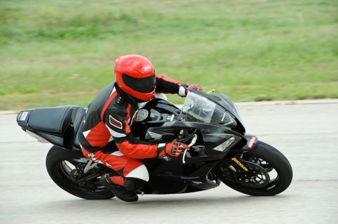 2001 Kawasaki KZ1000-A1 - Rider in full gear maneuvers a black sportbike on a paved track with grassy background.