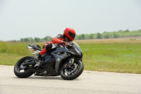 2001 Kawasaki KZ1000-A1 - Rider on a black sportbike navigates a turn on a track with grassy fields in the background.