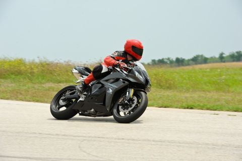 2001 Kawasaki KZ1000-A1 - A rider on a black sportbike navigates a turn on a track, with grassy fields in the background.