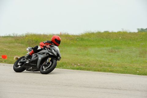 2001 Kawasaki KZ1000-A1 - A motorcycle rider leans into a turn on a paved track with grassy hills in the background.