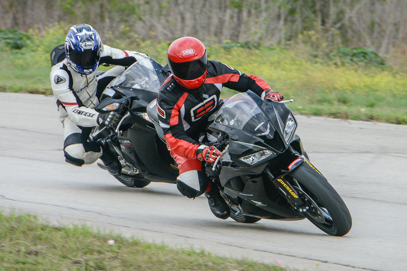 Two black sport motorcycles on a paved track, one in front of the other, with riders in racing leathers