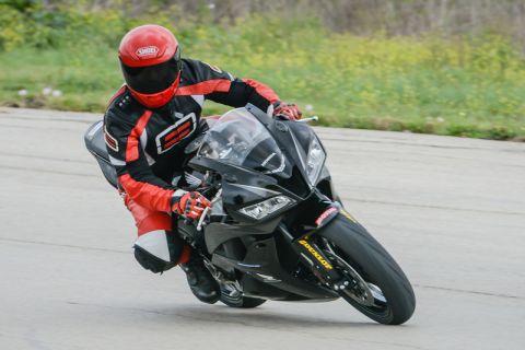 2001 Kawasaki KZ1000-A1 - A rider in full racing gear leans a black sportbike through a corner on a track.