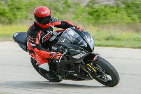 2001 Kawasaki KZ1000-A1 - Rider on a black sportbike navigates a track corner, wearing full racing leathers and a red helmet.