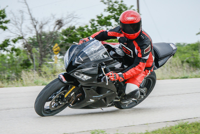 Black motorcycle with rider in red and black gear, leaning into a turn on a paved road