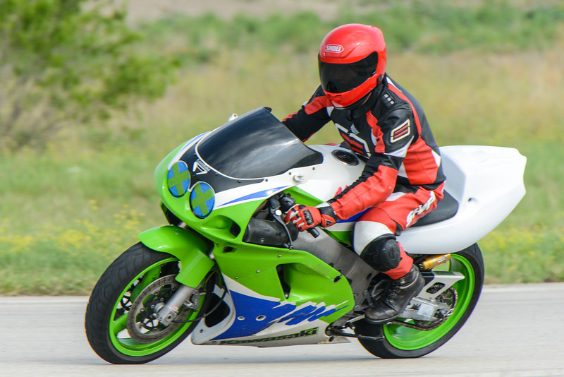 Rider in red and black gear on a green and white sportbike, with green wheels