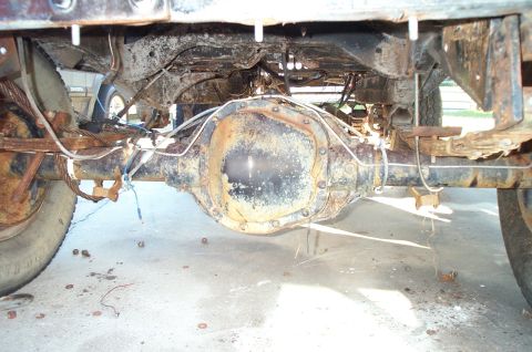 1995 Ford Bronco - The heavily rusted rear axle assembly of a vehicle is shown from underneath, with suspension components and brake lines visible.