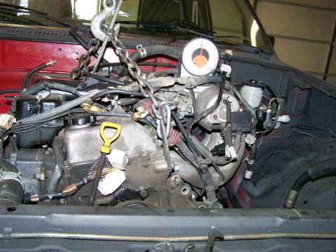 1988 Suzuki Samurai - Engine bay with hoist chains, a gauge, and wiring. Red vehicle interior visible.