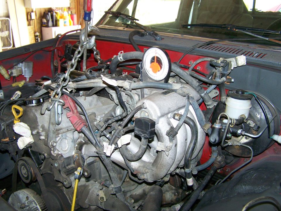 Engine being lifted out of a vehicle with a chain hoist. A pressure gauge is attached to the engine