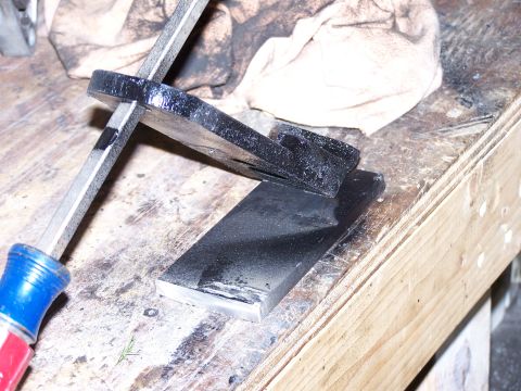 1988 Suzuki Samurai - A black metal part is clamped to a workbench, with a screwdriver holding it in place.