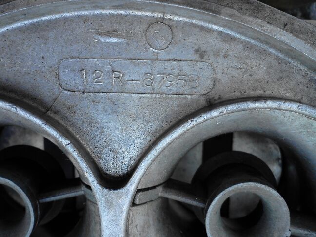 Close-up of a metal carburetor casting with part number 12R-8795B stamped into it