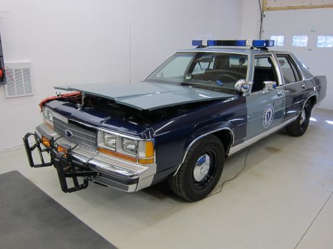 1991 Ford LTD Crown Victoria - 1991 Ford Crown Victoria LTD police car, two-tone blue and grey, with its hood open, parked indoors.